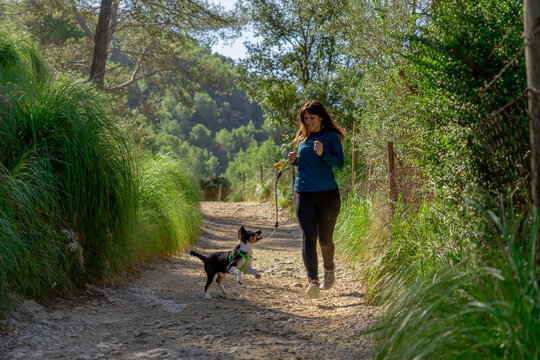 Young woman with fair skin and dark hair running with her dog along winding stone path in the mountain wearing sportswear.
