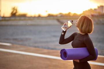 side view on young sportswoman going to take a sip of water outdoors after yoga exercises or...