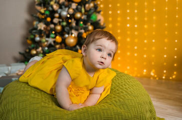 portrait of a baby girl in a yellow dress lying on a pillow on the background of a Christmas tree