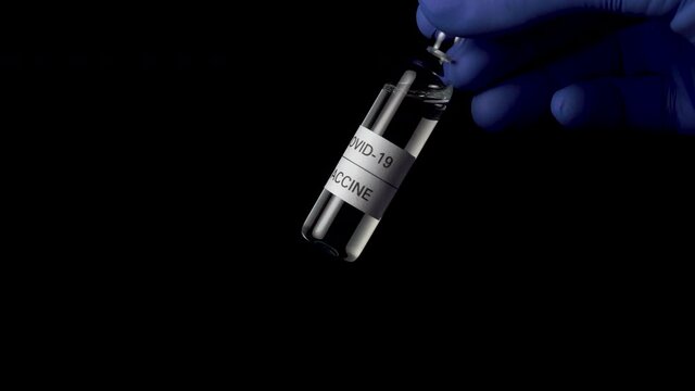 Coronavirus vaccine prototype, COVID-19. Ampoule with injection composition closeup in the hand of a researcher in blue medical gloves on a black background