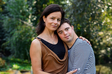 Portrait of down syndrome adult man with mother standing outdoors in garden. - obrazy, fototapety, plakaty