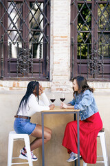 Obraz premium Two women drinking red wine sitting at a table outside a bar.