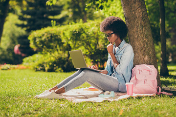 Full length body side profile photo of black skinned serious girl reading on laptop touching chin outside the city park wearing spectacles