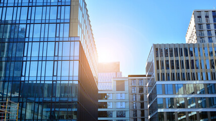 Blue curtain wall made of toned glass and steel constructions under blue sky. A fragment of a building. Glass facades on a bright sunny day with sunbeams in the blue sky.