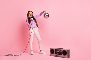 Full length photo of little kid girl sing song mic hold disco ball with boom box isolated over pastel color background © deagreez