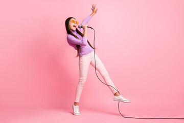 Full length photo of small kid girl sing song in mic wear violet jumper trousers isolated over...