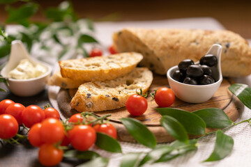 Fresh ciabatta bread with black olives, cherry tomatoes, cream cheese, leaf, wooden cutting board, home kitchen, Italian food concept, antipasto. Traditional snack, copy space, selective focus.