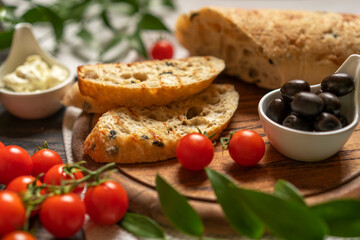 Fresh ciabatta bread with black olives, cherry tomatoes, cream cheese, leaf, wooden cutting board, home kitchen, Italian food concept, antipasto. Traditional snack, copy space, selective focus.