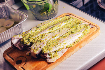 Raw pollock fillet with green sauce on a wooden cutting board in the kitchen