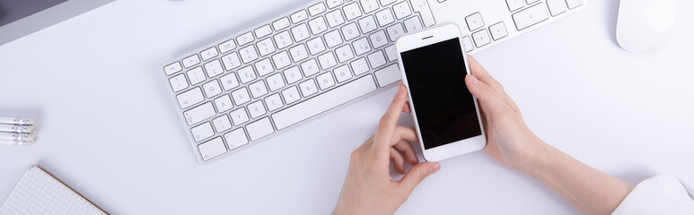 top view of female hands using smartphone over desktop with computer and stationery, work concept . High quality photo