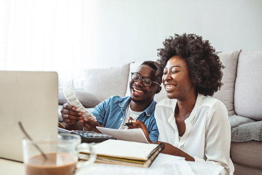 Happy Couple With Laptop Spending Time Together At Home. Happy Young Couple Paying Bills Together And Managing Budget, Sitting On The Sofa And Using Calculator And Laptop