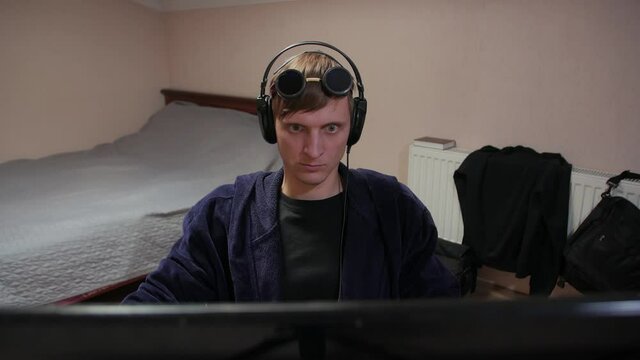 Funny man working at the computer expressive playing video games in sun glasses headphones at home
