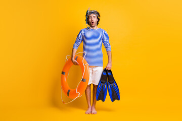 Full length photo of amazed barefoot guy hold life buoy flippers wear scuba mask goggles isolated on yellow color background © deagreez