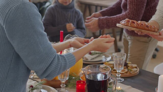 PAN mid-section of female hands giving tasty pie on wooden plate to unrecognizable woman while helping set dinner table on Christmas