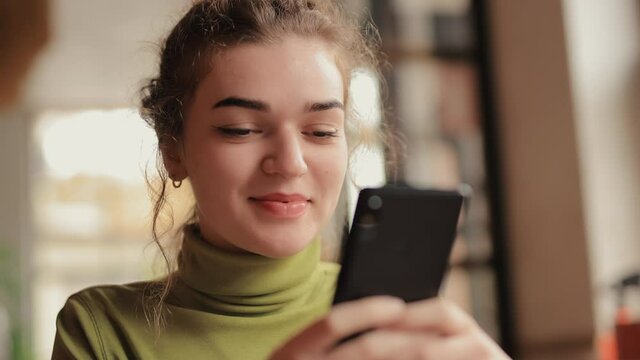 Woman using mobile phone sitting in a cafe texting sms or browsing website