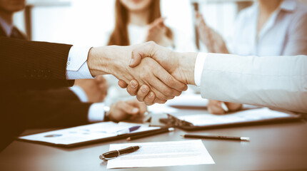 Business people shaking hands at meeting while theirs colleagues clapping and applauding. Group of unknown businessmen and women in modern white office. Success teamwork, partnership and handshake