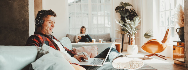 Happy couple at home. Husband and wife sitting on the couch and watching TV series on laptop,...