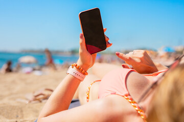 Woman using mobile phone while relaxing on the beach in hot summer day