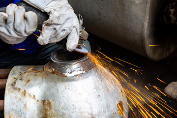 Worker grinding the metal valve with an electric grinder in the workshop. Selective focus to the working area. Workers wear leather gloves to prevent work hazards.