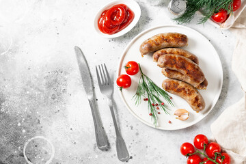 Fried sausages. Fried sausages with spices, sauce, tomatoes and parsley. Delicious meat sausages in a white ceramic plate on a light gray table. German dish	