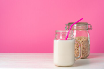 Oat milk in glassware and dry oat flakes on pink background