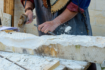 Detail of artist's hands sculpting marble with hammer and chisel