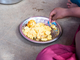 Unidentified poor classmates children with uniforms sitting on the floor outdoors, eating with their right hand some rice with masala. Lunch time