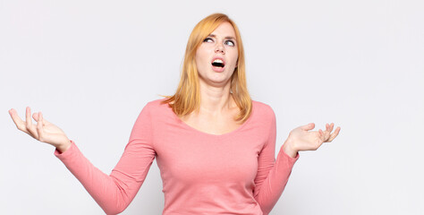 red head pretty woman shrugging with a dumb, crazy, confused, puzzled expression, feeling annoyed...