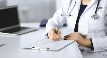 Unknown woman-doctor is prescribing some medication for her patient, using a clipboard, while...