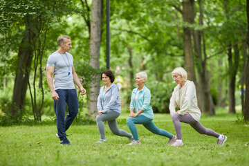 Wide shot of three good-looking senior women having workout in city park with trainer looking at them