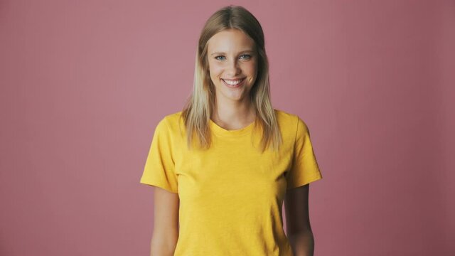 A beautiful blonde woman is doing hello gesture standing isolated over a pink background in the studio