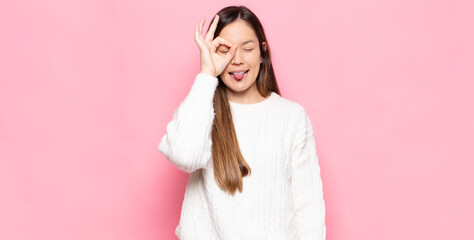 young pretty woman smiling happily with funny face, joking and looking through peephole, spying on...
