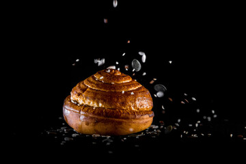 A bread roll with seeds falling from the top on black background