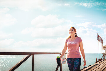 Sea and freedom. Adult woman in sportswear with a shaker in her hands, walking along the pier pier....