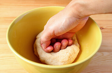Closeup of man's hand kneading bread dough in a mixing bowl