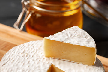 Cheese pieces and honey jar served on dark table