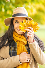 Good looking woman holds colorful autumn leaves in front of one of her eyes on a chilly fall day