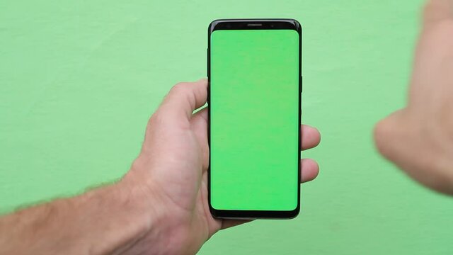 close up of man hand using smartphone with empty green screen mock up finger swiping chroma-key display internet searching app