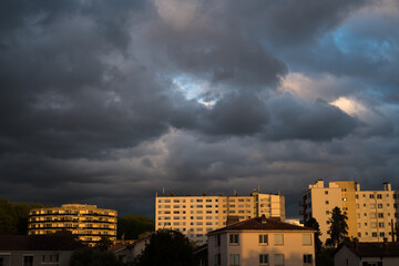 Fototapeta na wymiar bâtiments d'une ville sous un ciel nuageux et sombre, illuminés et colorés en jaune par un coucher de soleil 