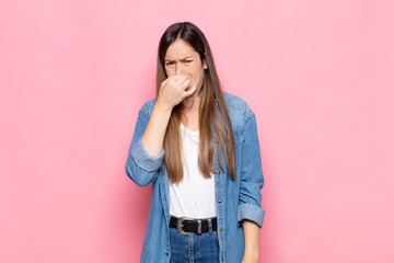 young pretty woman feeling disgusted, holding nose to avoid smelling a foul and unpleasant stench