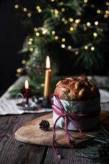 Christmas still life with decorated Panettone, lit candles and lights on pine branches on dark background.