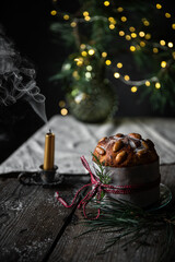 Christmas still life with homemade Panettone decorated as gift, blown candle and lights on pine branches on wooden table.