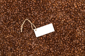 Granos de café enteros junto a una cartela blanco sin escribir. Vista superior y de cerca. Copy...