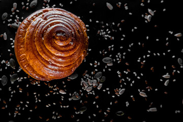 A bread roll with seeds on black background. Top view. Flatlay