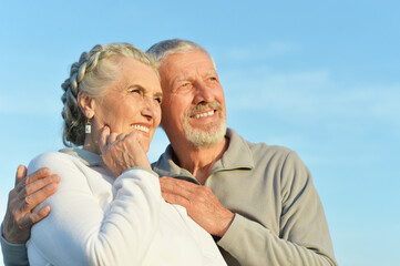 Obraz premium Happy senior couple hugging against blue sky