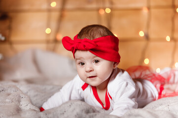 Cute baby girl in red bow on head and white sweater lying on blanket, a Christmas background in a studio with Christmas scenery