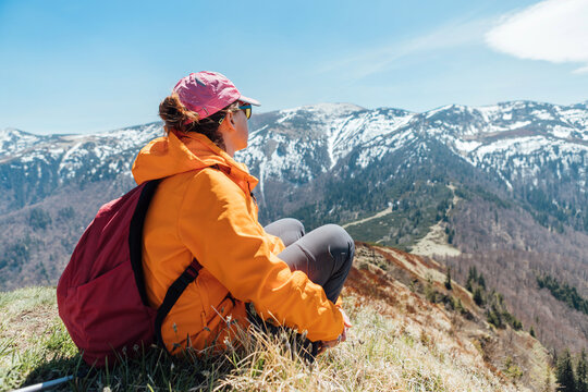 Dressed bright orange jacket backpacker woman sitting on the hill enjoying green valley at Mala Fatra mountain range,Slovakia. Active people and European hiking tourism concept image.