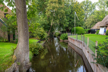 Fototapeta na wymiar A canal flowing between buildings in a famous village in the Netherlands, visible trees and flowers in the gardens.