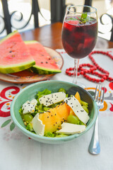 Holiday celebration table setting with food. Melon salad with grapes and cheese served with a glass of red fruit wine.