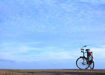 Fototapeta premium Bicycle parked on cobble stone road against magnificent blue sky over calm expanse on a sunny day. Netherlands. Minimalist image